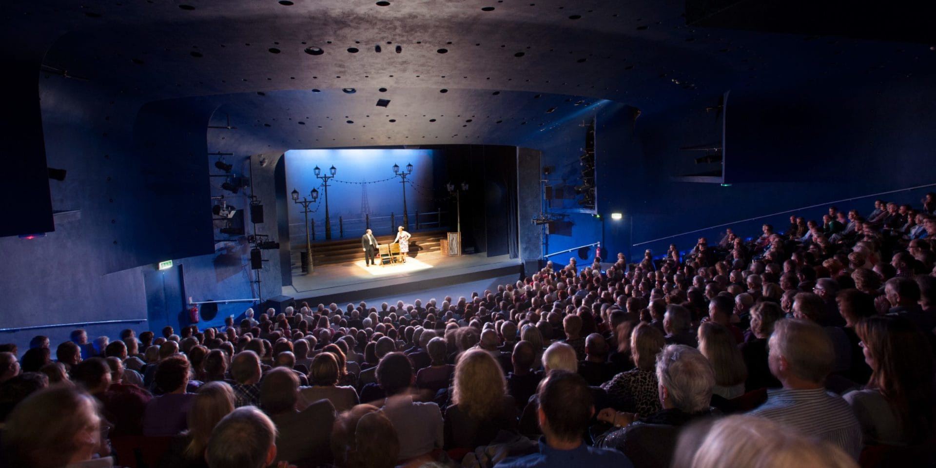 A full auditorium of people watching a performance on the main Derby Theatre stage.