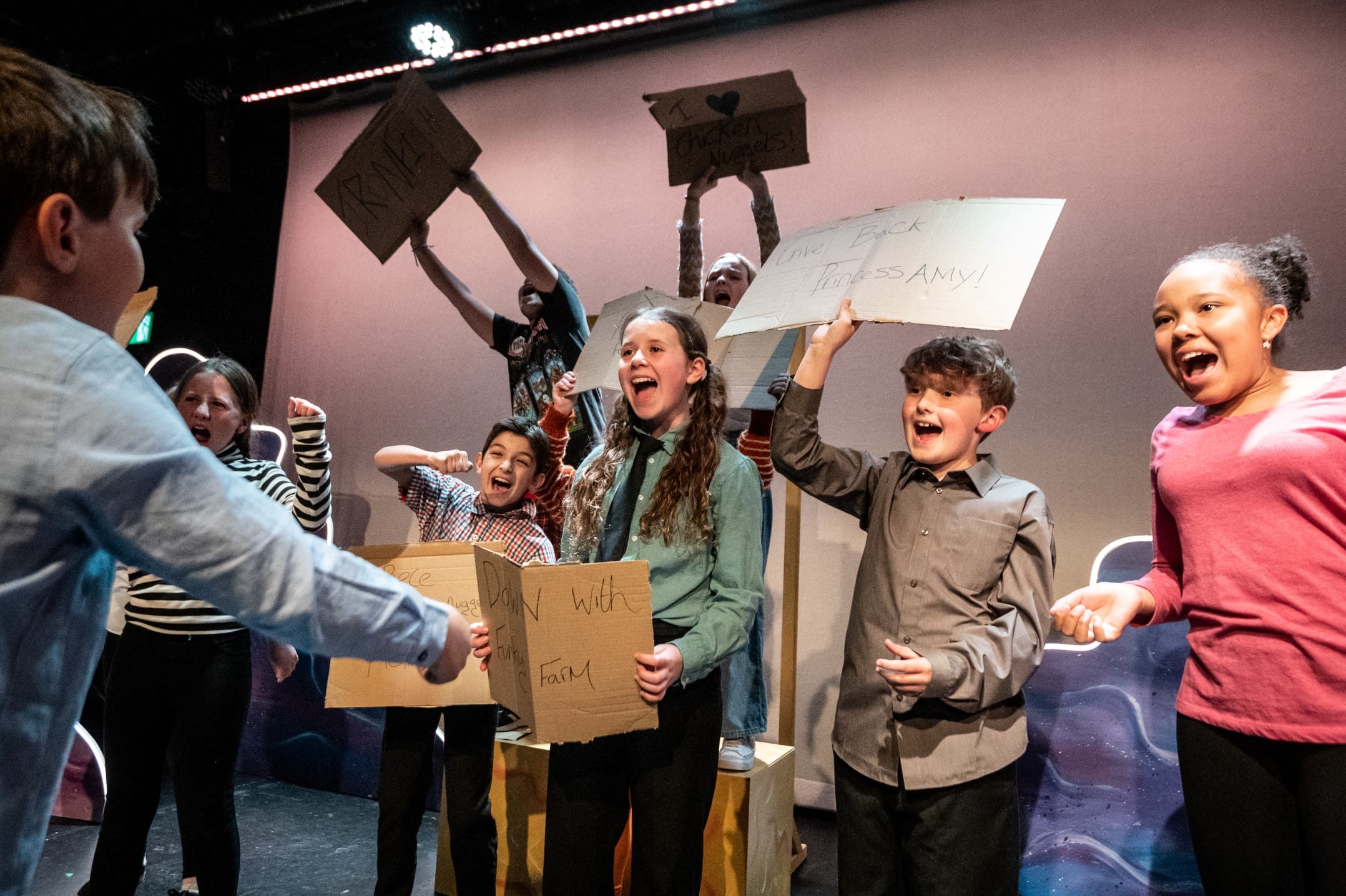 A group of children enthusiastically perform on stage in a youth theatre production of 