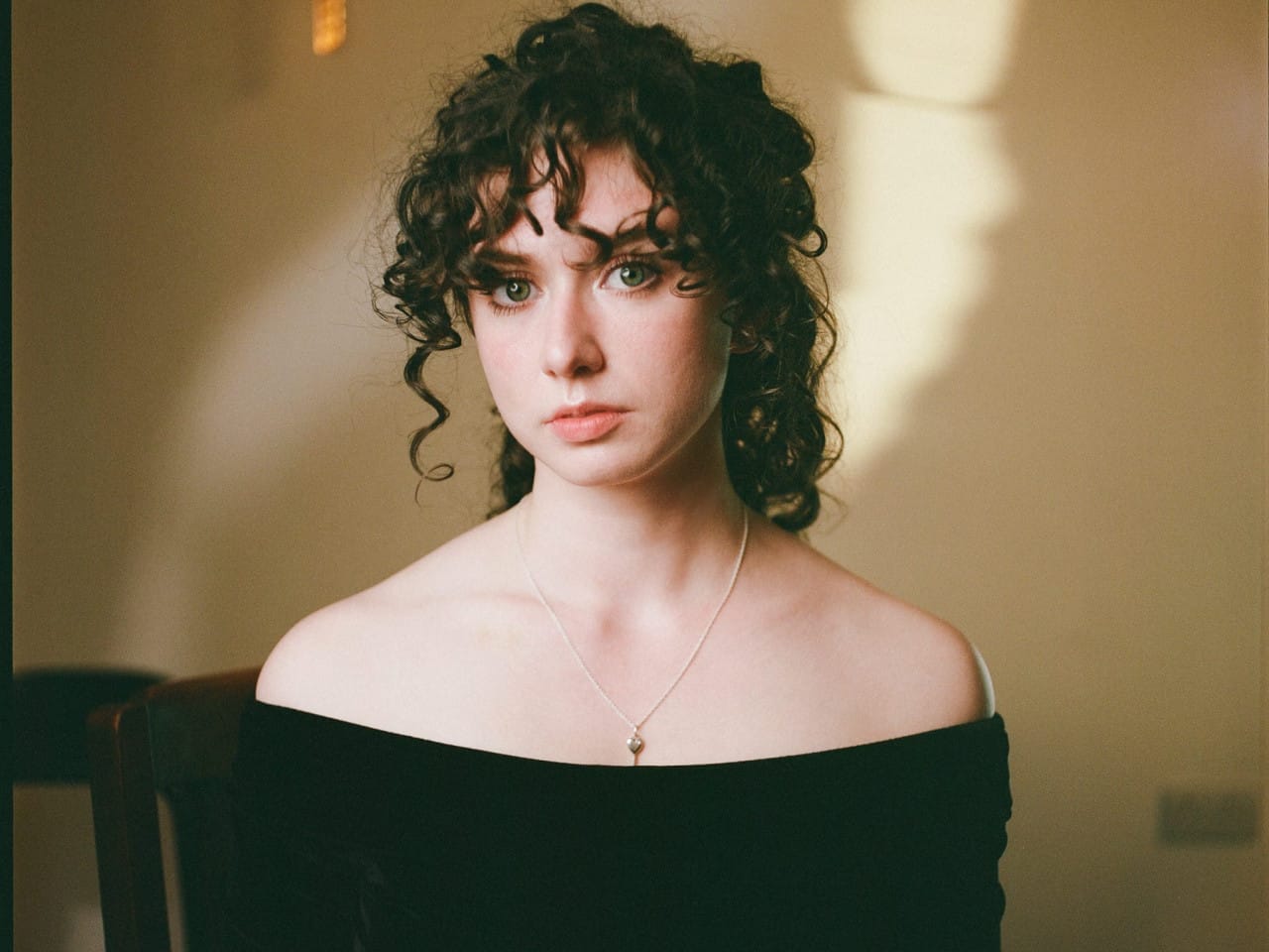 Performer's headshot with black curly hair and black off the shoulder top