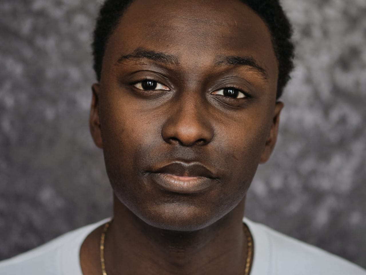 Performer’s headshot - low cut black hair, gold chain and white t shirt