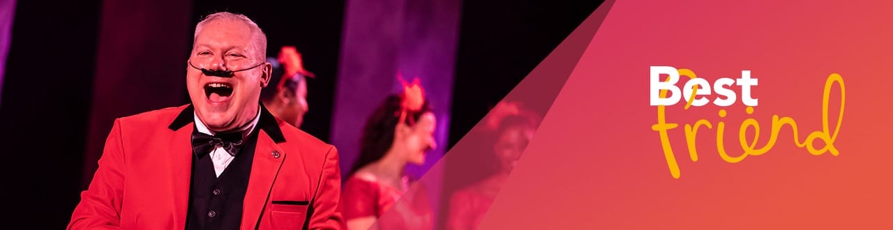 Joyful man in a red suit and bow tie laughing on stage, with blurred dancers in matching red costumes in the background. Overlay text on the right says “Best friend” in white and yellow on a pinkish-orange gradient background.